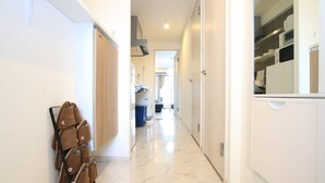 A hallway with a shoe rack, a kitchen area with appliances, and a bathroom visible in the distance. - Prosper Rainbow Villa (Osaka)