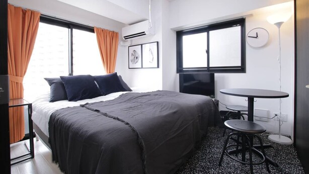 Una habitación de hotel moderna con una cama grande, una mesita, un televisor y una ventana con cortinas.