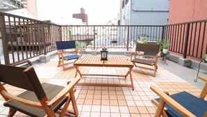 A rooftop terrace with wooden furniture and a tiled floor, surrounded by a metal railing. - Sky Terrace Kujyo (Osaka)