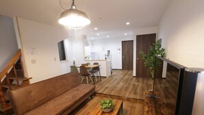 A modern living room with a brown sofa, wooden coffee table, and a hanging light fixture. - Sky Terrace Kujyo (Osaka)