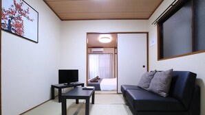 Ein kleines, möbliertes Zimmer mit einer Couch, einem Fernseher und einem Bett im Hintergrund.