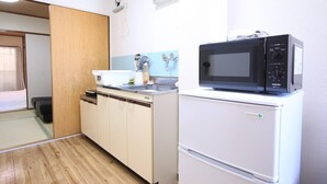 Eine kleine Küche mit einer Mikrowelle und einem Kühlschrank, Holzboden und einer Schiebetür zu einem Schlafbereich.
