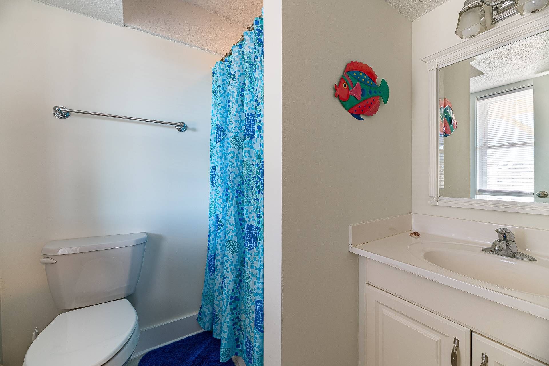 A bathroom with a toilet, a shower curtain, a sink, and a mirror.