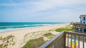 A beach with a wooden deck and colorful chairs, overlooking the ocean. - Sun Trippin' | Oceanfront Escape in South Nags Head with Private Beach Access & Panoramic Views (South Nags Head)