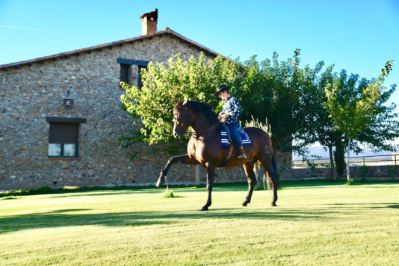 Une personne à cheval devant un bâtiment en pierre doté d’une fenêtre et d’une porte.