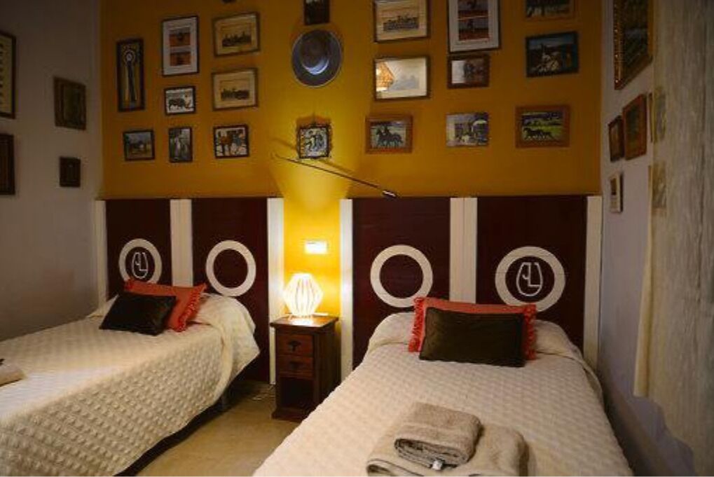 Une chambre avec deux lits, chacun doté d’une tête de lit ronde et d’une table de chevet. Les murs sont décorés de tableaux encadrés.