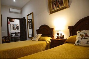 A hotel room with two beds, a nightstand with a lamp, a mirror, and a painting on the wall. - Casa Rural Yeguada Jimenez Latorre (Fernán Caballero)