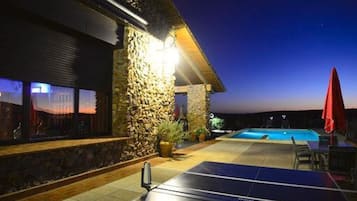A pool area with a stone wall, a red umbrella, and a solar-powered table.