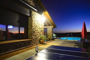 A pool area with a stone wall, a red umbrella, and a solar-powered table. - Casa Rural Yeguada Jimenez Latorre (Fernán Caballero)