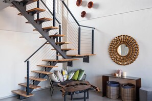 A modern interior with a spiral staircase, a round mirror, and a console table with decorative items. - The Bond Square (Durban)