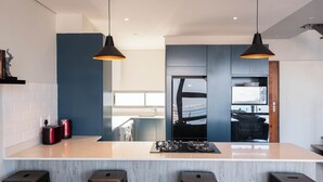 A modern kitchen with a central island, two pendant lights, and a view into the dining area. - The Bond Square (Durban)