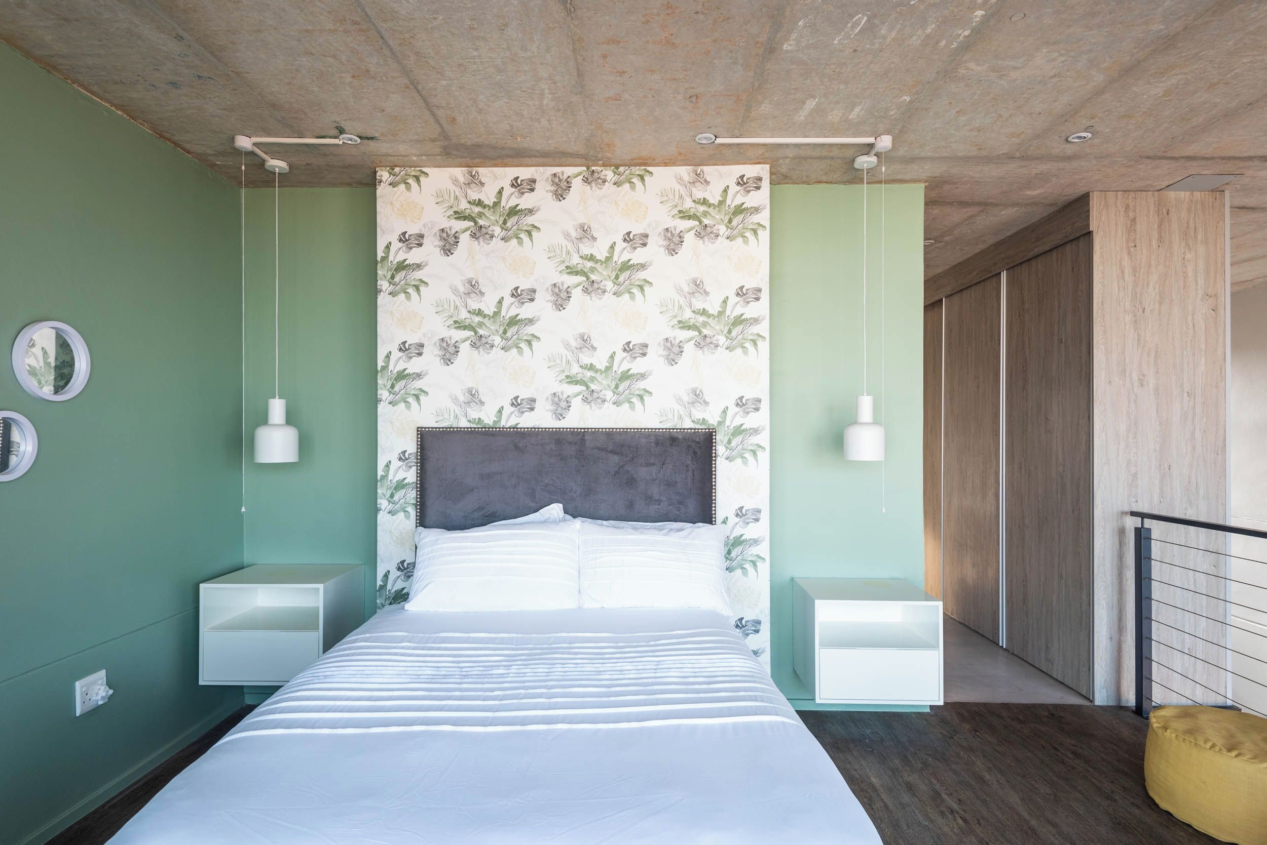 A modern bedroom with a large bed, two bedside tables, a headboard with floral wallpaper, and a wooden ceiling.