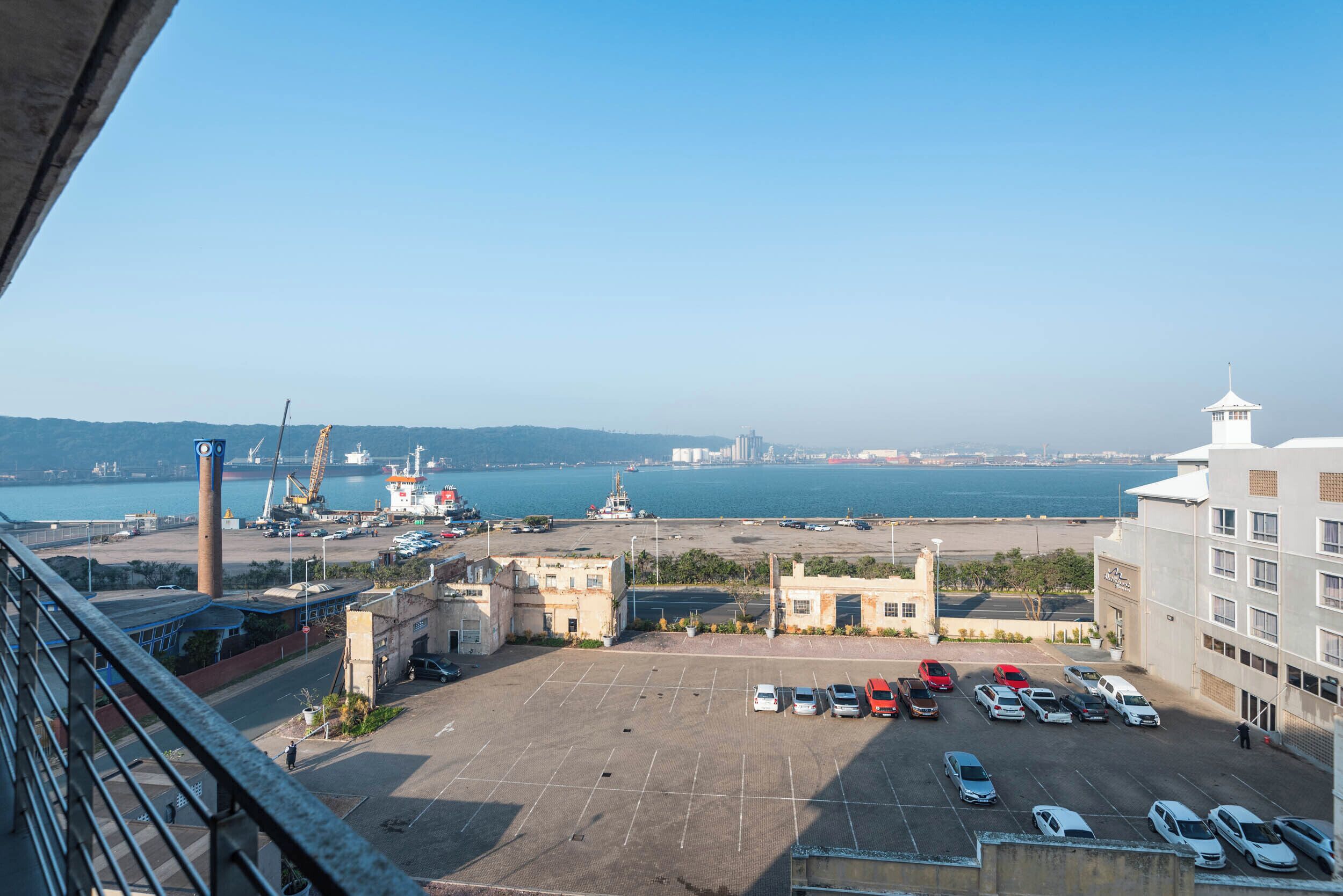 A parking lot with several cars, a crane, and a body of water in the background.