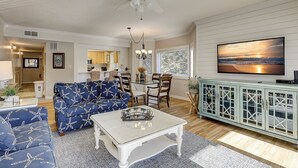 A spacious living room with a ceiling fan, a dining area with a chandelier, and a large TV mounted on the wall.