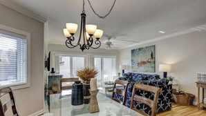 A dining area with a glass-top table, wooden chairs, a chandelier, and a ceiling fan.