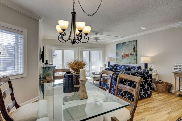 A dining area with a glass-top table, wooden chairs, a chandelier, and a ceiling fan.