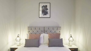 A neatly made bed with a tufted headboard, two bedside tables with lamps, and a framed artwork above the bed. - Host & Stay | The Normanby (Whitby)