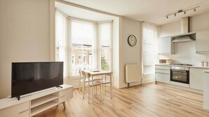 A modern kitchen with a stove, oven, and white cabinetry. There is a dining table with chairs and a flat-screen TV on a white stand. - Host & Stay | The Normanby (Whitby)