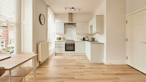 A modern kitchen with white cabinets, a built-in oven, and a dining area with a wooden table and chairs. - Host & Stay | The Normanby (Whitby)