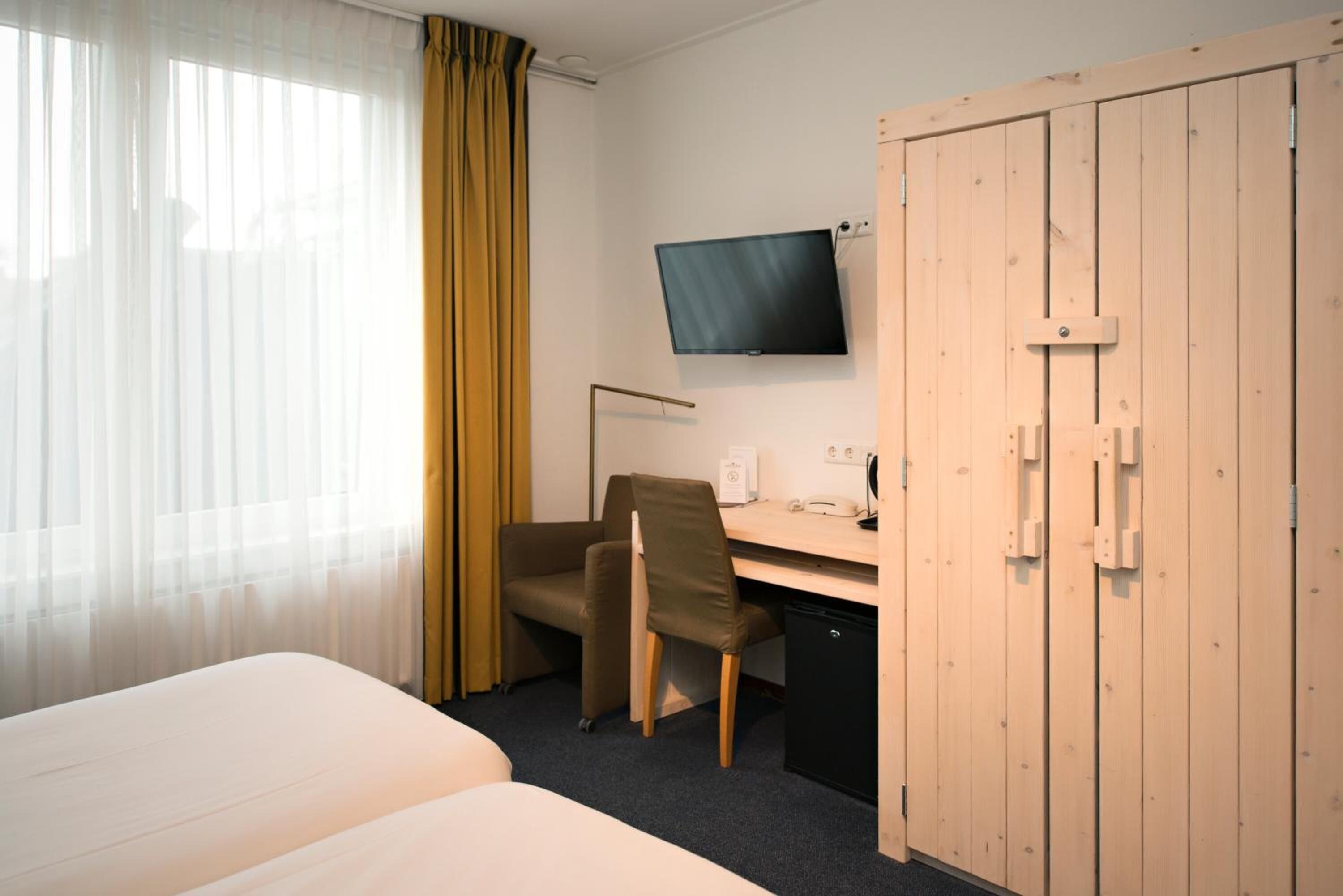 Ein Hotelzimmer mit einem Bett, einem Schreibtisch mit Stuhl, einem an der Wand befestigten Fernseher und einem Kleiderschrank.