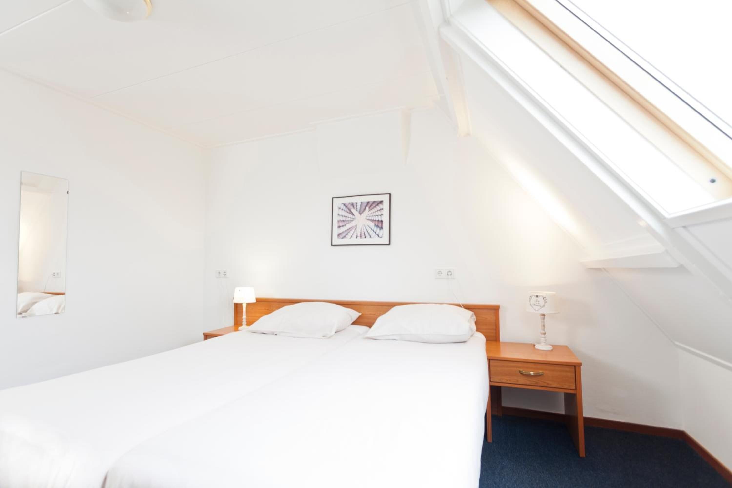 A hotel room with a single bed, a nightstand, a lamp, a wall-mounted picture, and a skylight.