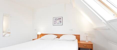 A hotel room with a single bed, a nightstand, a lamp, a wall-mounted picture, and a skylight.