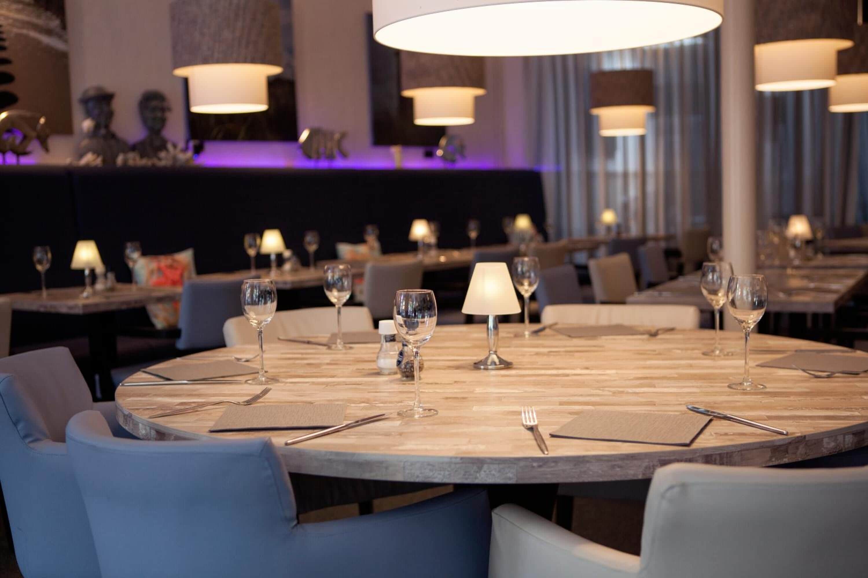 Un restaurante con mesas redondas, cada una dispuesta con copas de vino, cubiertos y servilletas.