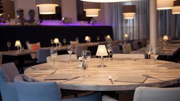 Un restaurante con mesas redondas, cada una dispuesta con copas de vino, cubiertos y servilletas.