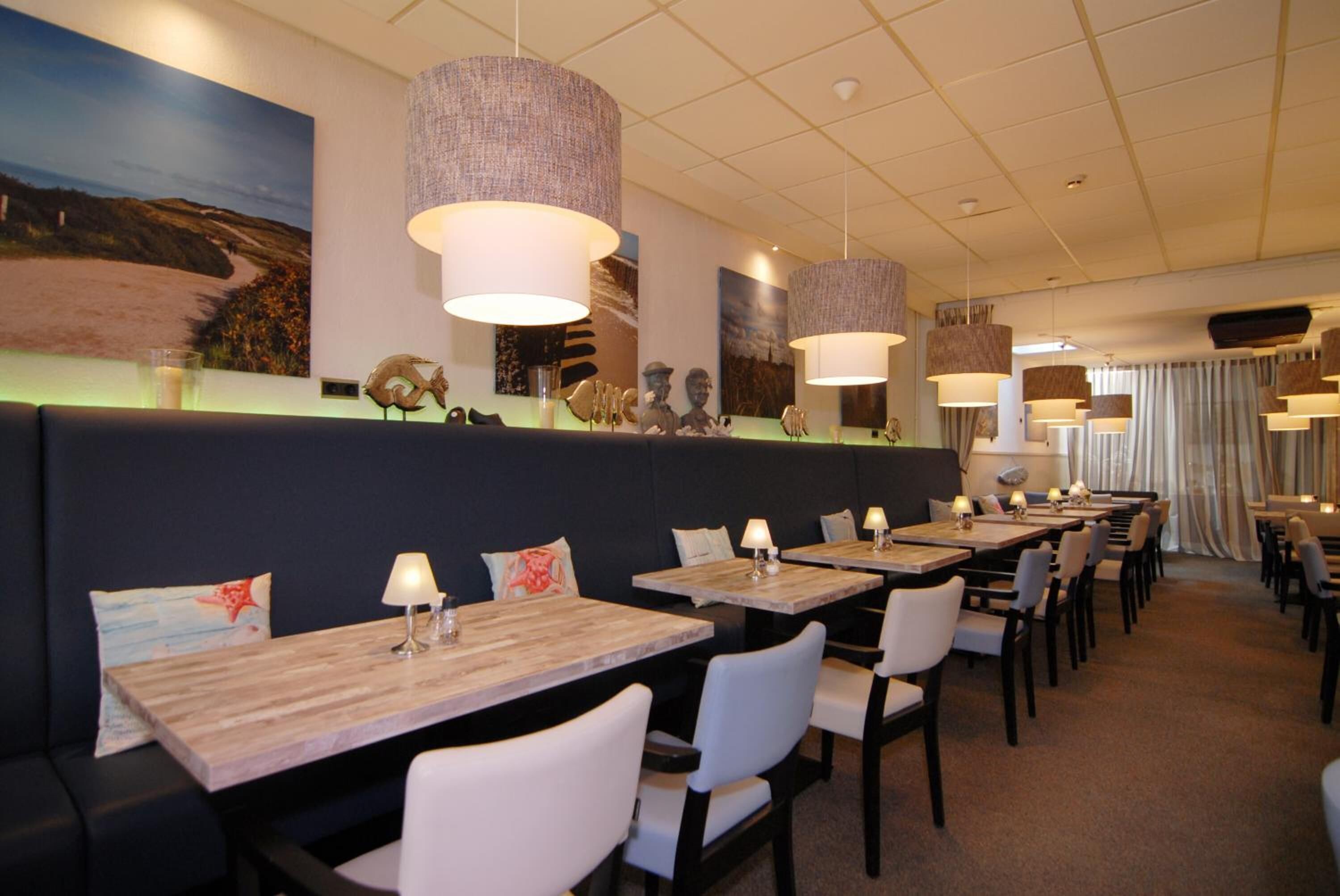 A restaurant with long wooden tables, white chairs, and hanging lamps.