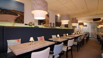 A restaurant with long wooden tables, white chairs, and hanging lamps.
