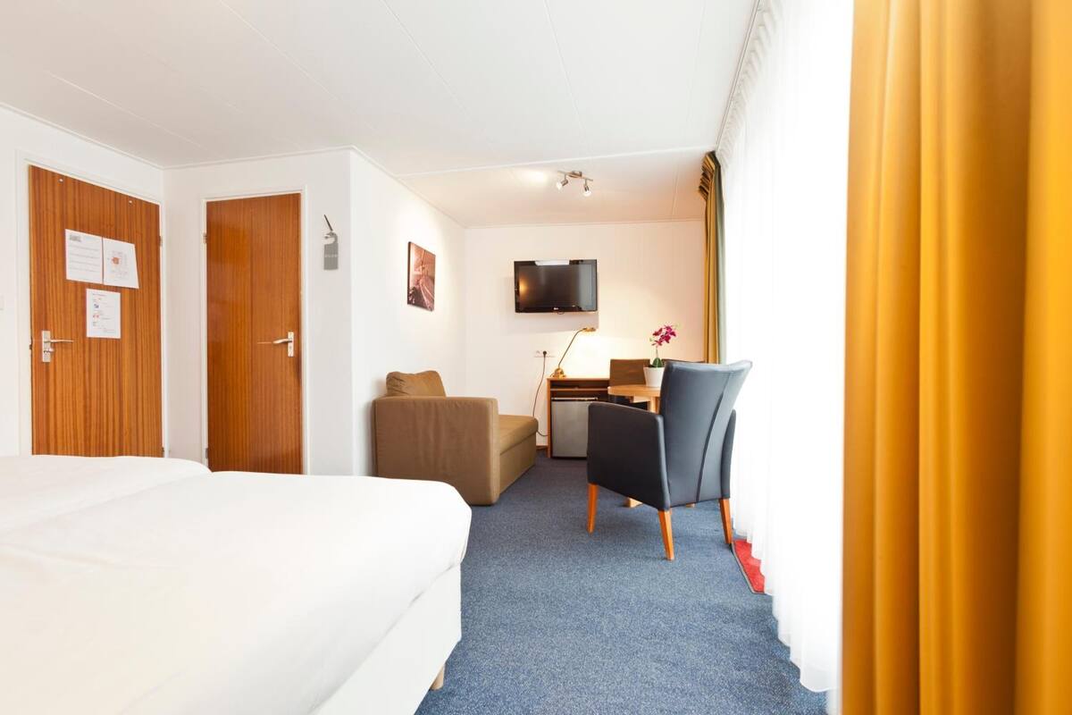 Ett hotellrum med en säng, ett skrivbord, en stol, en tv och en dörr.
