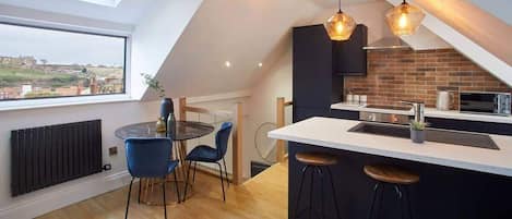 Une cuisine moderne dotée d’une verrière, un coin repas avec une table ronde et des chaises, et un bar avec des tabourets.