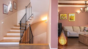 A staircase with a black railing, a living room with a beige sofa, two wall-mounted paintings, and a floor lamp. - Spacious  holiday house - pool / jacuzzi / sauna / playground / 8+2 (Rakalj)