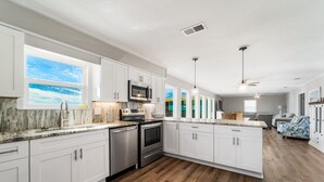 A modern kitchen with white cabinetry, stainless steel appliances, and a large window overlooking a scenic view.