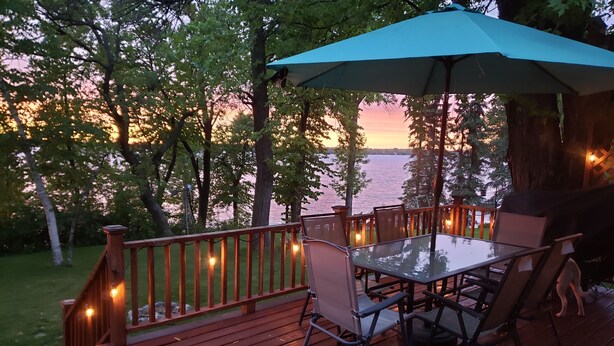 A deck with a glass table and chairs, surrounded by a wooden railing and string lights. - Lakeside Leisure: Relax, Recharge, Reconnect! (Alexandria)