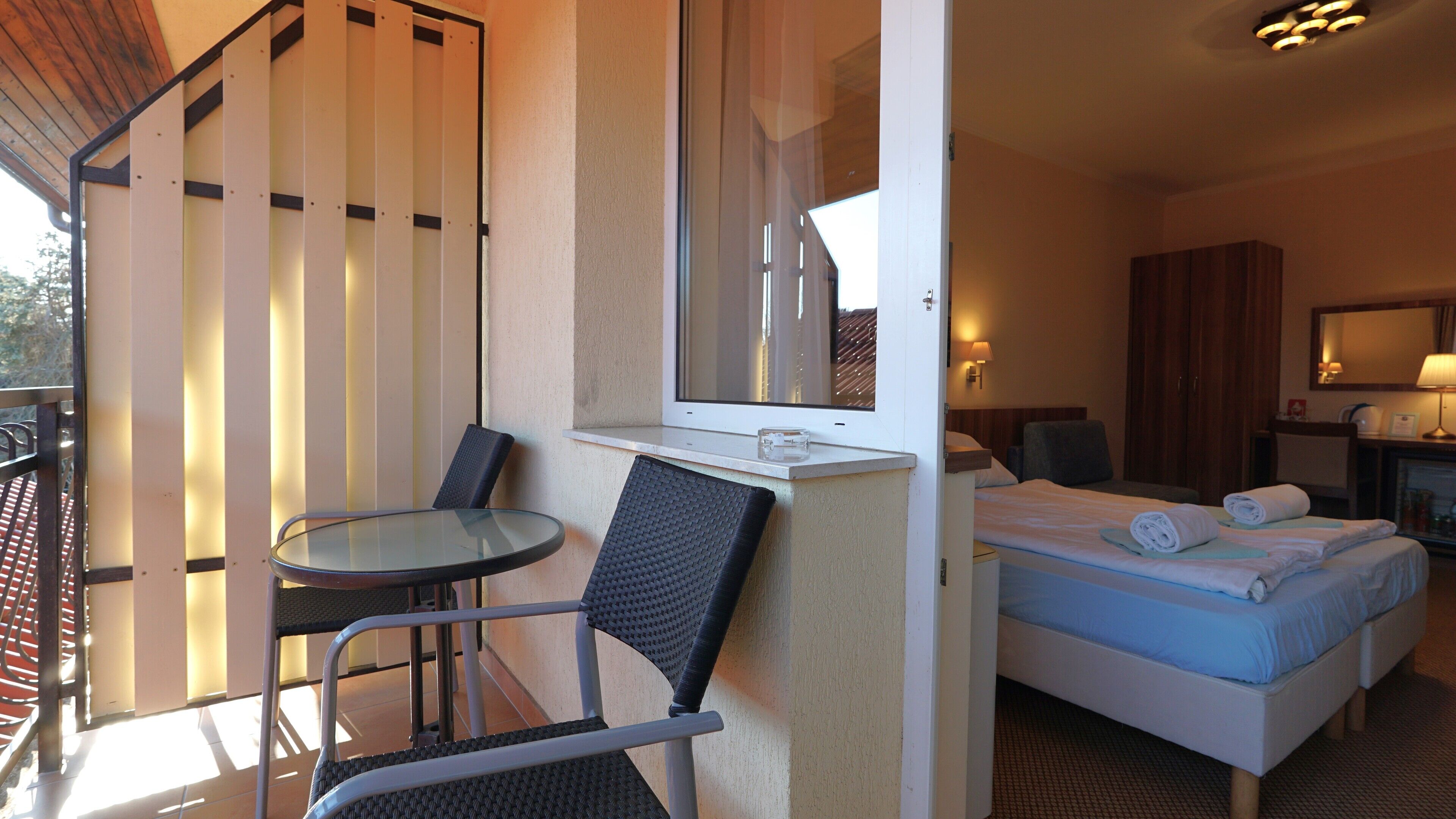 A hotel room with a balcony, a bed with towels, a small table, and a chair.