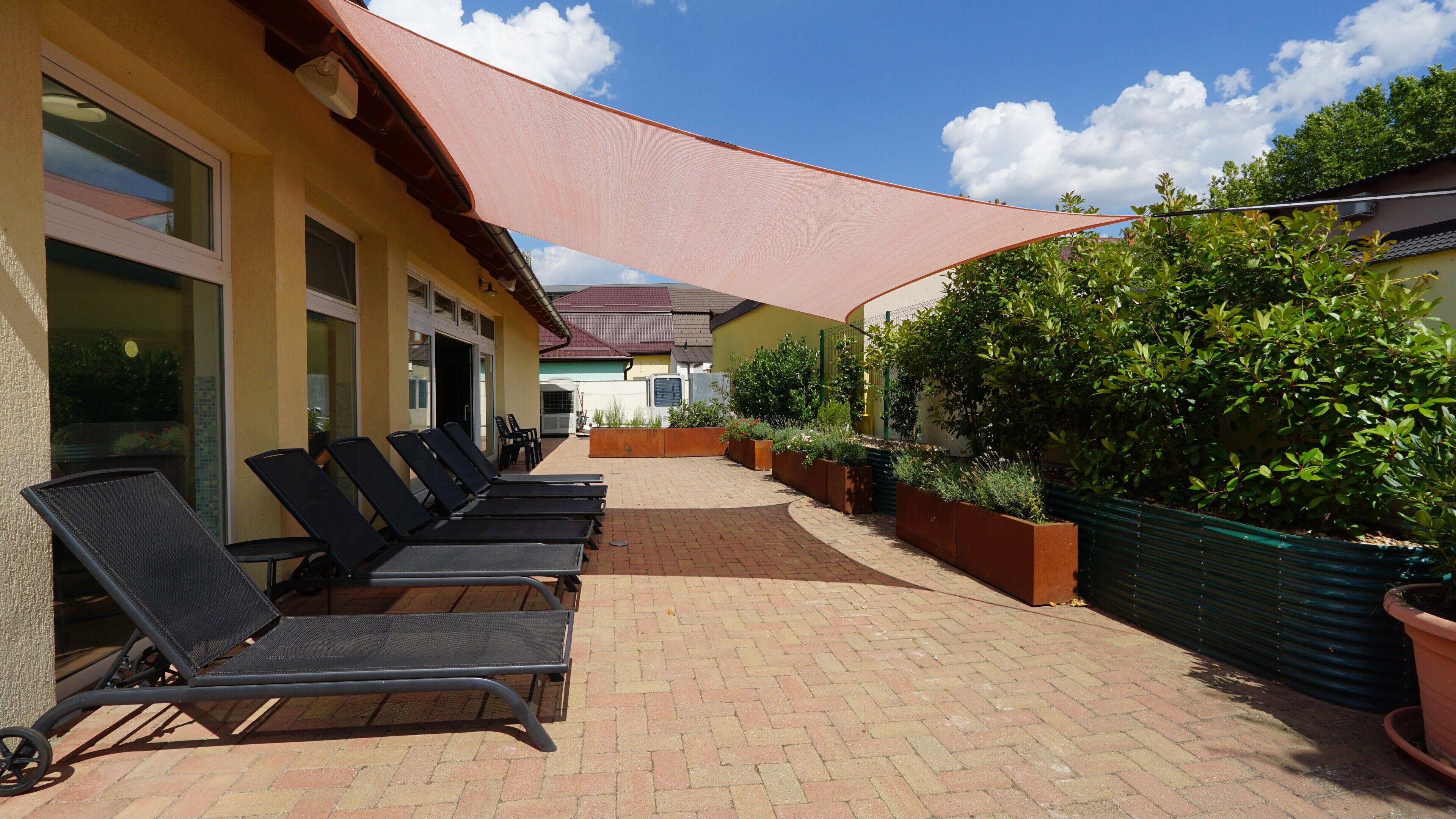 A patio with sun loungers, a brick pathway, and a shaded area with plants.