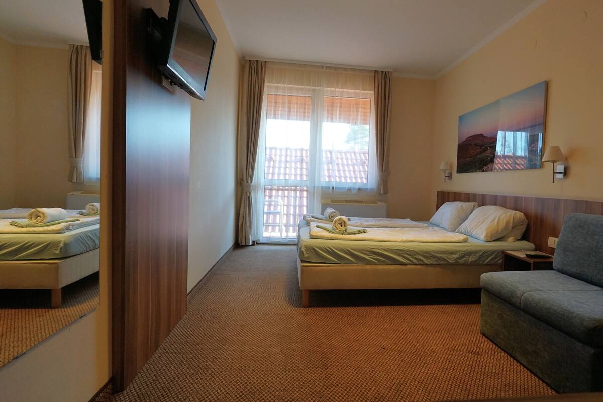 A hotel room with two beds, a sofa, a TV mounted on the wall, and a painting on the wall.