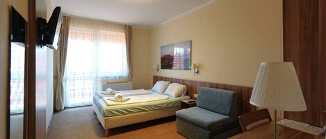 Una habitación de hotel con cama, escritorio, silla, lámpara, un cuadro en la pared y una ventana con cortinas.