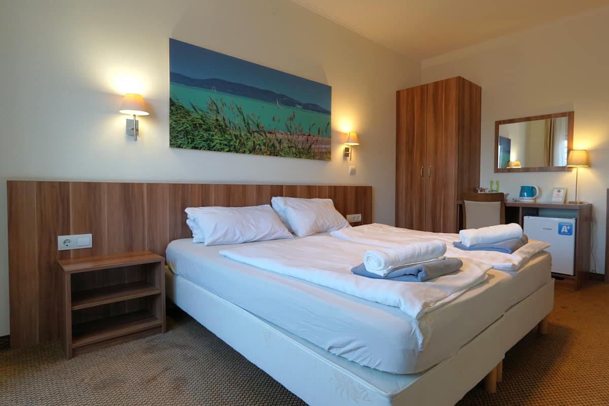 A hotel room with a large bed, a desk with a computer, a small fridge, and a painting on the wall.