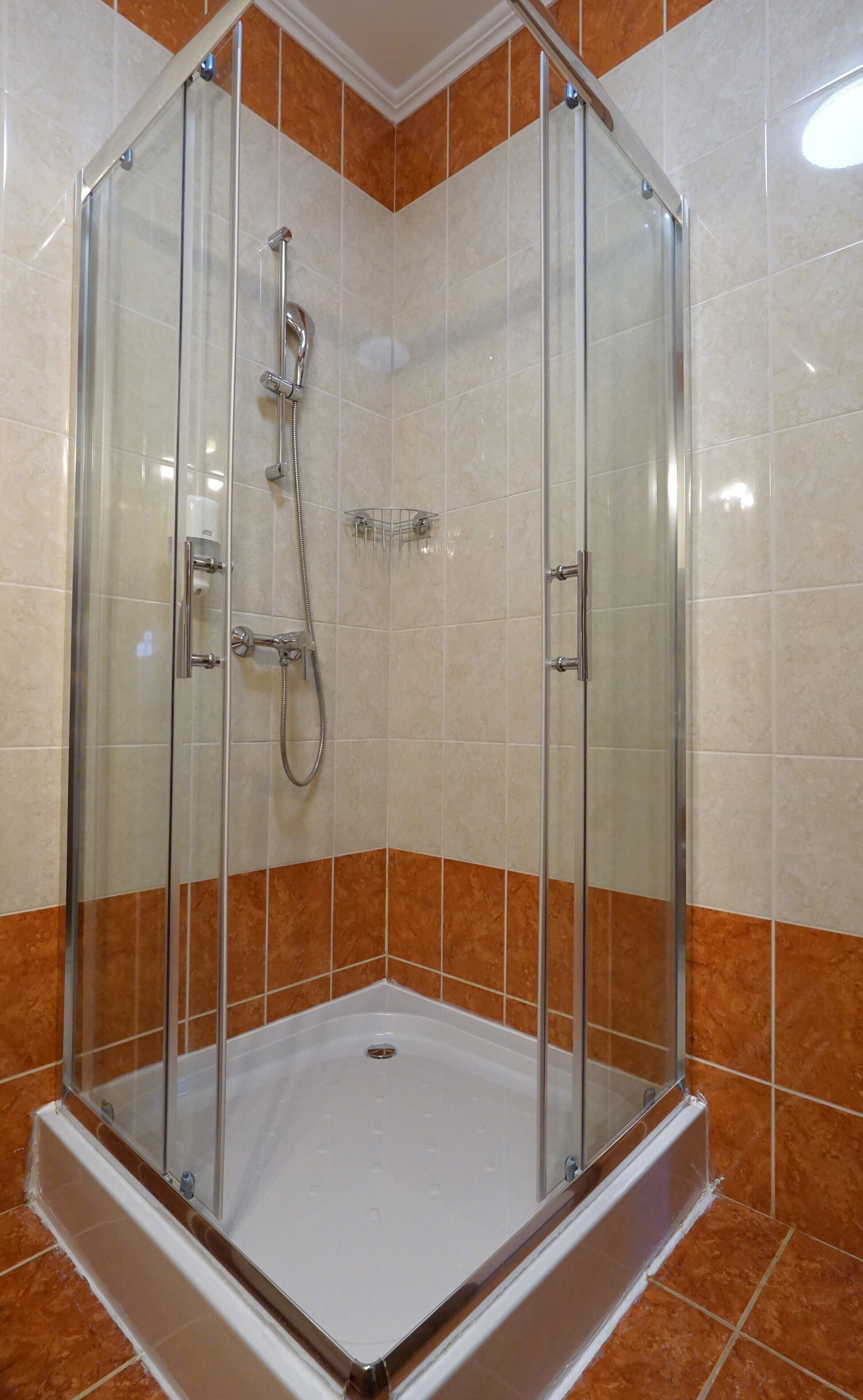 Une cabine de douche fermée par des parois de verre, avec un sol blanc et des murs recouverts de carreaux orange.