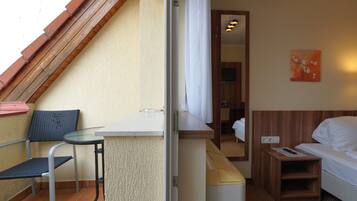 A hotel room with a balcony, a small table, a chair, a bed, and a painting on the wall.