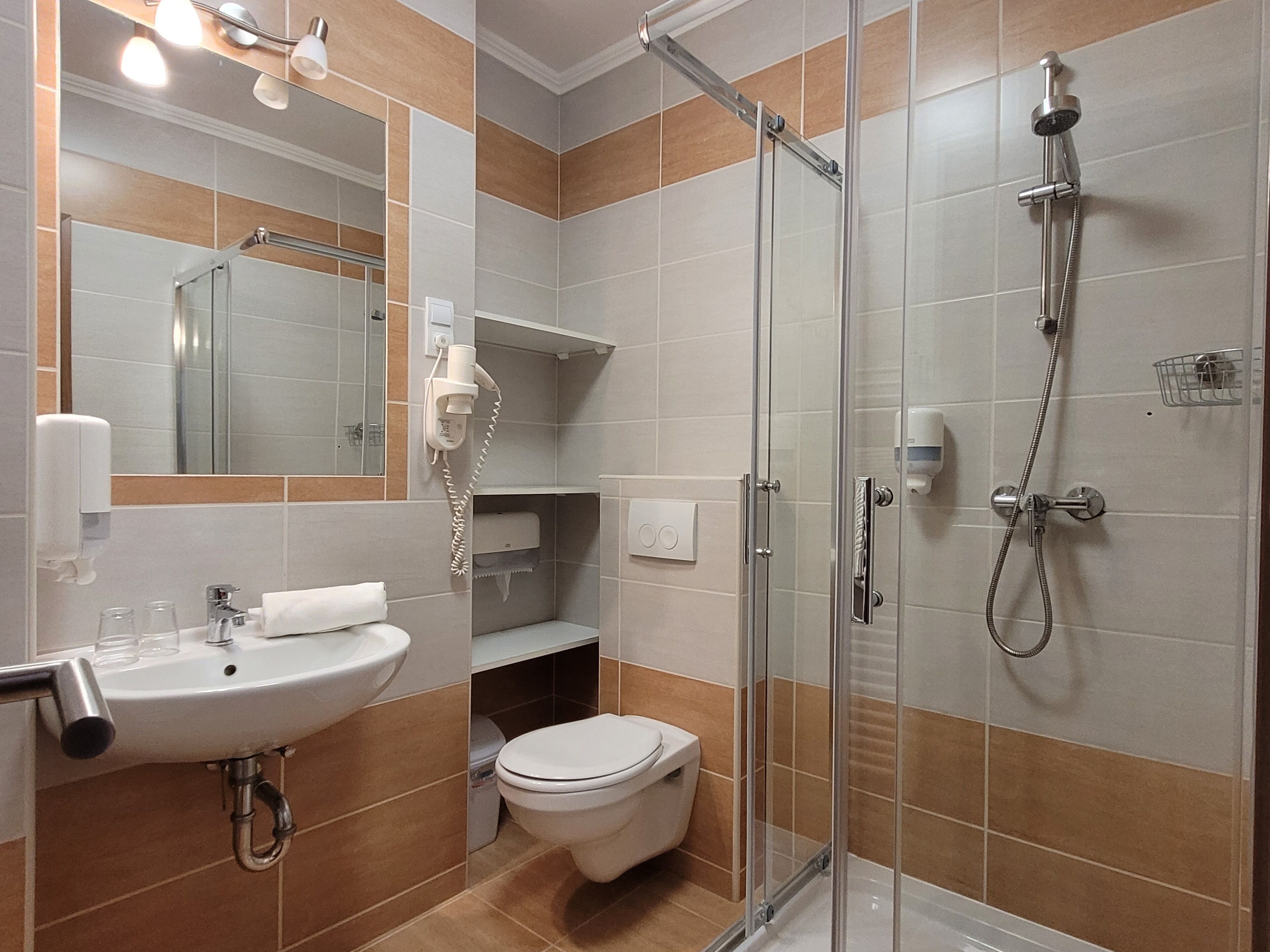 Ein modernes Badezimmer mit einer Duschkabine, einem Waschbecken inklusive Spiegel und einer Toilette.