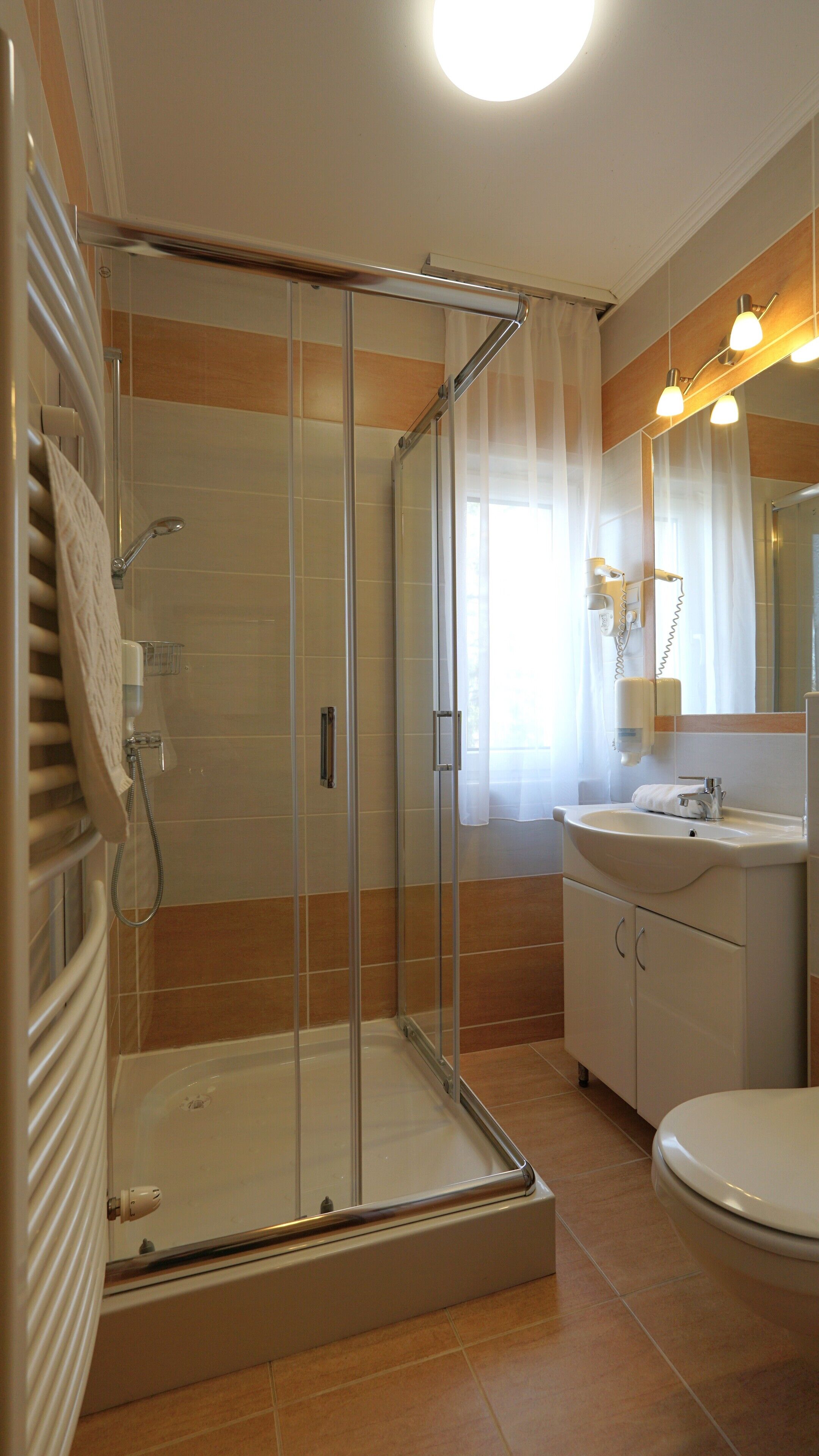 A bathroom with a glass-enclosed shower, a sink, a toilet, and a mirror with lights.