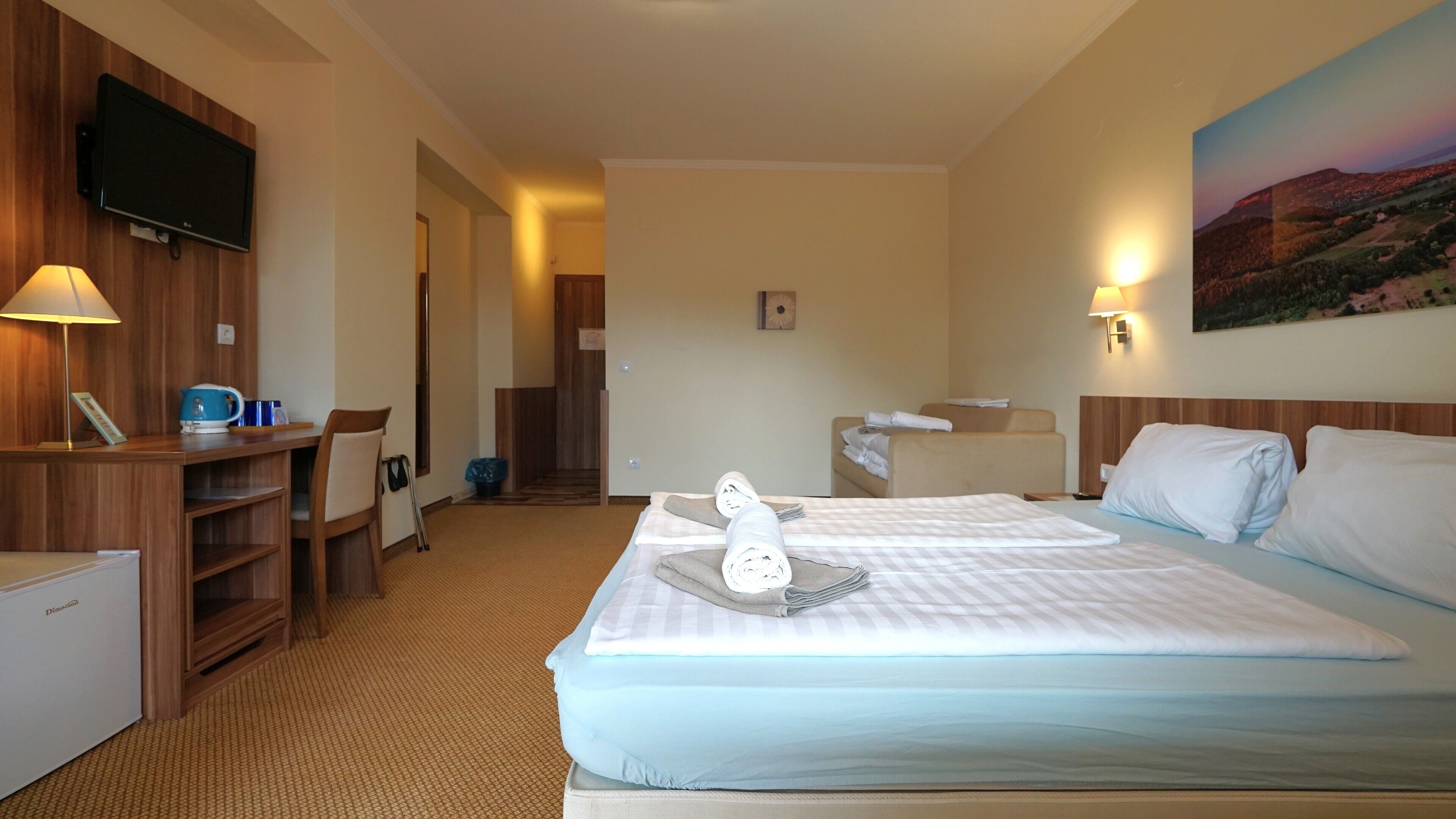 A hotel room with two beds, a desk, a television, and a painting on the wall.