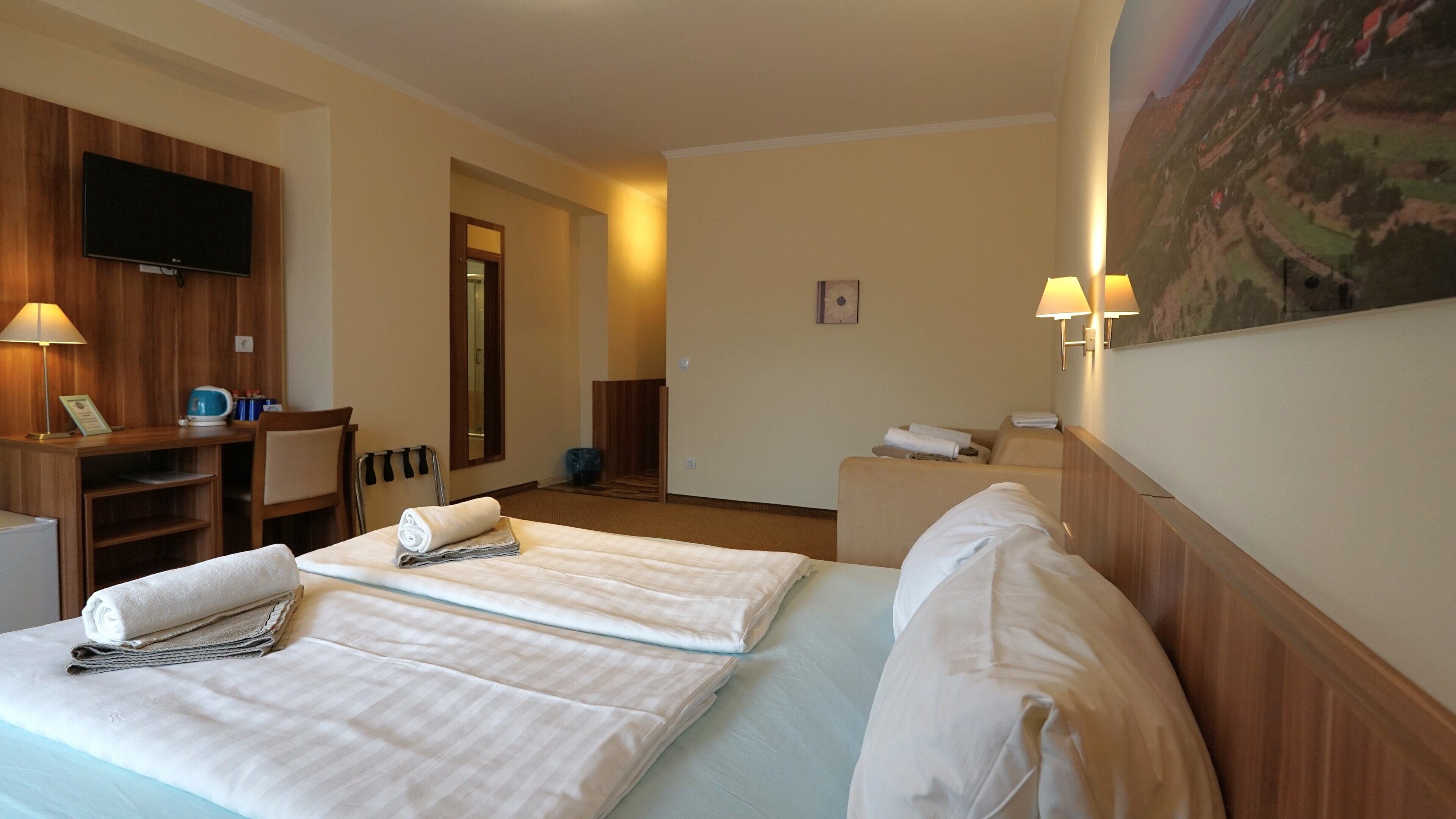 A hotel room with two beds, a desk, a television, and a painting on the wall.