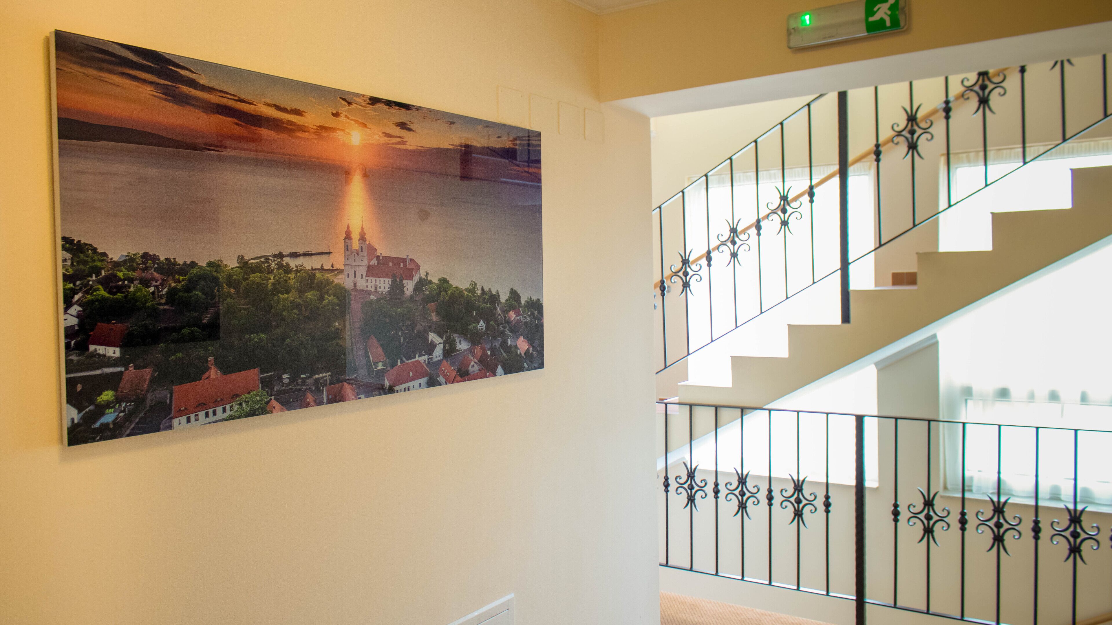 Una escalera con barandillas de metal ornamentadas y un cuadro grande de un castillo en la pared.