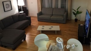 A modern living room with a grey sofa, a small coffee table, and a TV on a stand. - Hunsaker Suite, Reading Serviced Apartment (Reading)