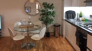 A modern kitchen with a round mirror, a dining table with chairs, a potted plant, and a built-in stove. - Hunsaker Suite, Reading Serviced Apartment (Reading)