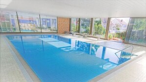 An indoor swimming pool with clear glass walls, a tiled floor, and a bench along the wall. - Landgasthof Hirsch (Remshalden)